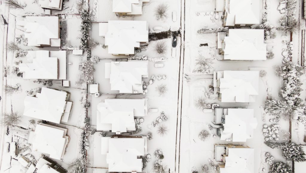Aerial view of a suburban city after a snow storm, houses and streets blanketed in snow.