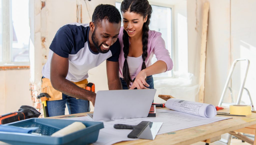 A smiling contractor reviews potential rebates on laptop with homeowner.
