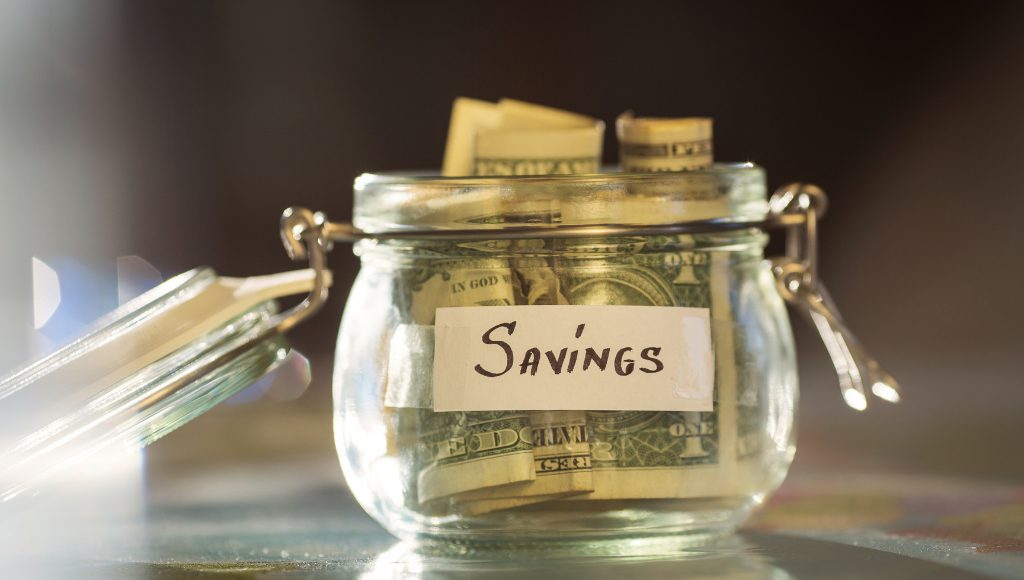 A glass jar with the word "savings" on it, filled with dollar bills.