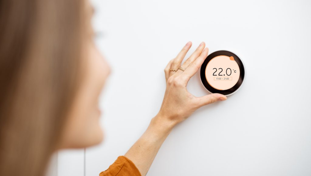 A woman adjusts a smart home thermostat for energy savings.