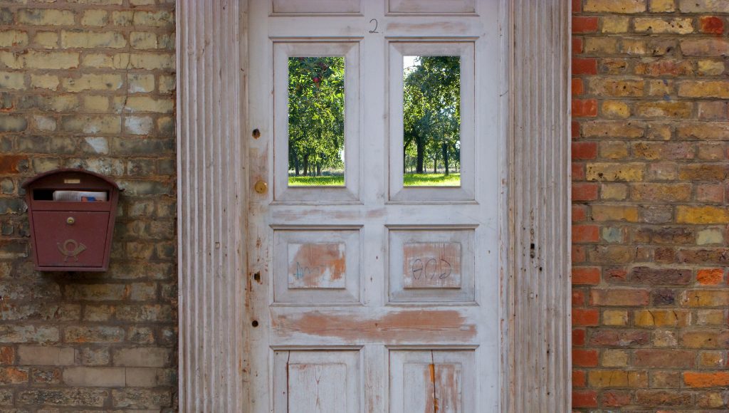 An old, weathered door, scratched, warped, and stripped of paint, on the front of a brick building.