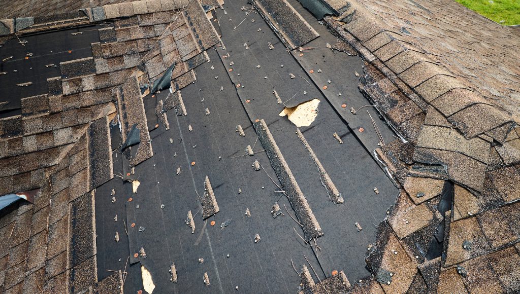 A roof with many damaged and missing shingles viewable from the ground.