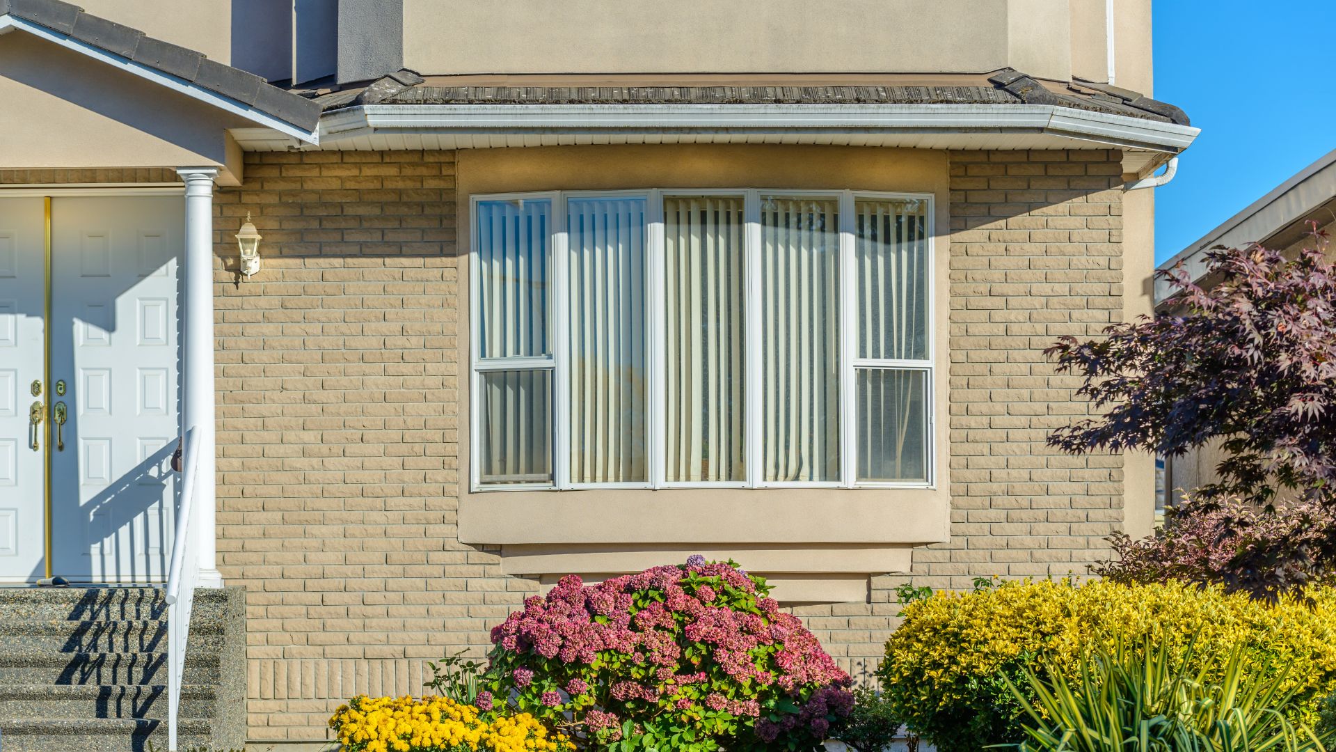 A large, five-pane bay window on the front of a beige brick suburban home.